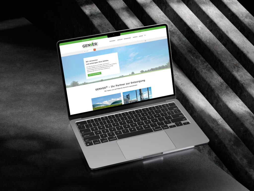 Ein Laptop, auf dem die GENVER-Website angezeigt wird, steht auf einer dunklen, strukturierten Betonfläche mit diagonalen Licht- und Schattenmustern im Hintergrund.