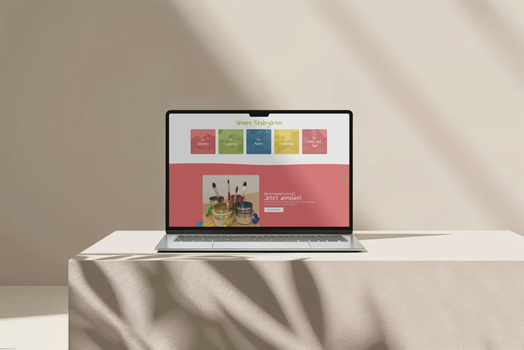 Ein Laptop auf einem beigefarbenen, mit Stoff bezogenen Tisch zeigt die farbenfrohe Familienzentrum Heek Website Referenz mit den Rubriken Bibliothek, Veranstaltungen, Cafeteria und Familien, darunter ein Bild mit Farbtöpfen und Pinseln.