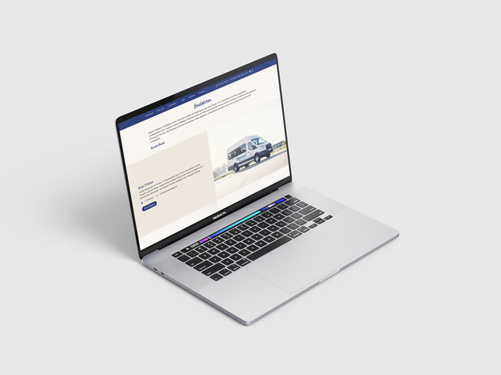 Ein silberner MacBook-Laptop auf einer weißen Oberfläche zeigt die Website von Fragemanns Reisekutsche mit marineblauen und weißen Farben, Text und dem Bild eines Lieferwagens auf einer offenen Straße. Der Laptop-Bildschirm ist nach links geneigt.