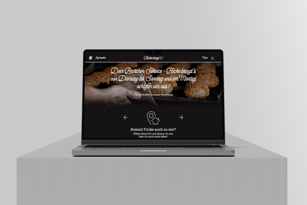 Ein Laptop auf einer grauen Plattform zeigt die Fricke bringt's Website Referenz, mit einer Nahaufnahme von Händen, die Brot halten, und einem deutschen Text, der für frische Backwaren wirbt. Der Hintergrund ist schlicht und hellgrau.