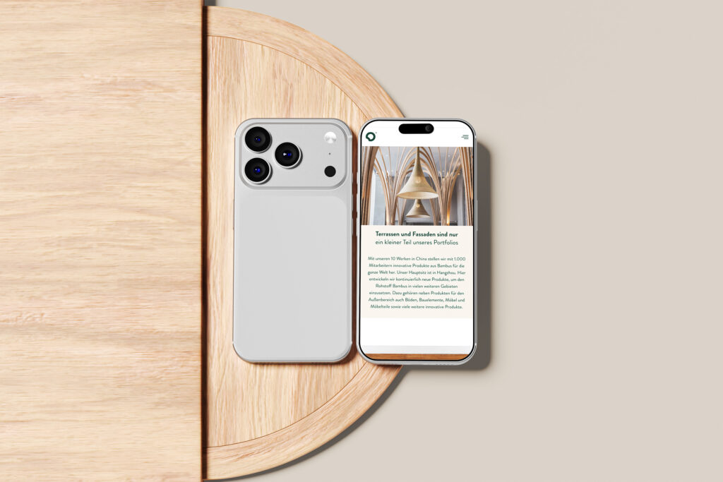 Auf einem runden Holztisch vor einem hellbeigen Hintergrund liegen zwei moderne Smartphones, von denen eines seine Rückseite zeigt und das andere die Dasso Bambus Website mit einem Glockenbild.