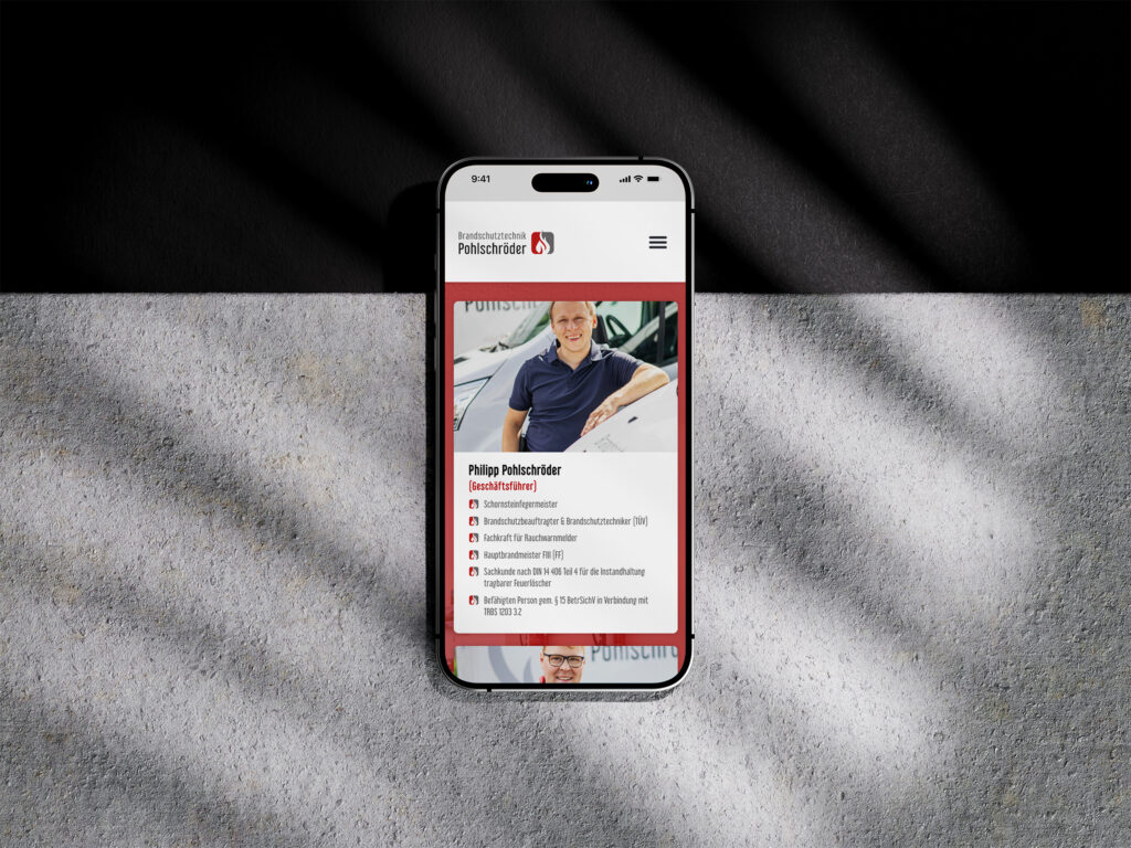 Ein Smartphone, auf dem das Profil der Brandschutztechnik Pohlschröder-Website einer lächelnden Person in einem blauen Hemd neben einem Auto angezeigt wird, mit Text und Symbolen darunter, platziert auf einer strukturierten Oberfläche mit diagonalen Schatten.