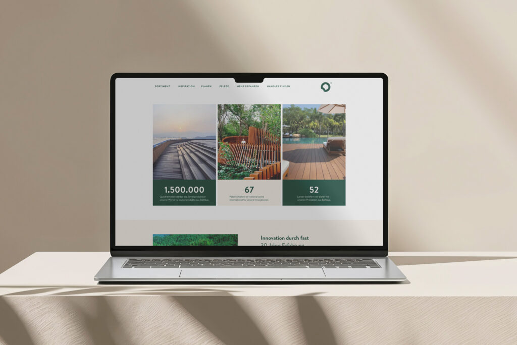 Ein Laptop auf einer beigen Oberfläche zeigt die Website von Dasso Bambus mit Bildern von Holzterrassen und Pools im Freien sowie Statistiken und Navigationslinks im oberen Bereich. Weiches natürliches Licht wirft Schatten auf den Hintergrund.