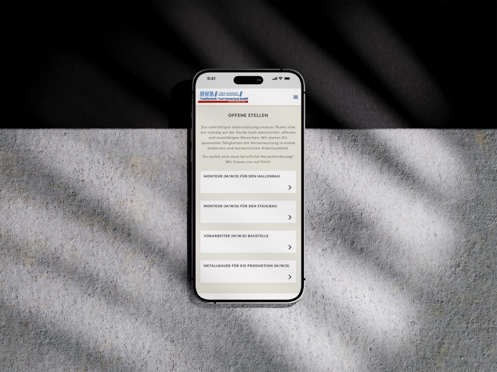 Ein Smartphone, das die Website der MWM Metalltechnik Westmünsterland in deutscher Sprache anzeigt, liegt auf einer strukturierten grauen Oberfläche unter diagonalen Schatten. Auf dem Bildschirm sind vier offene Stellen zu sehen, jede in einem separaten Kasten mit einem Pfeil.