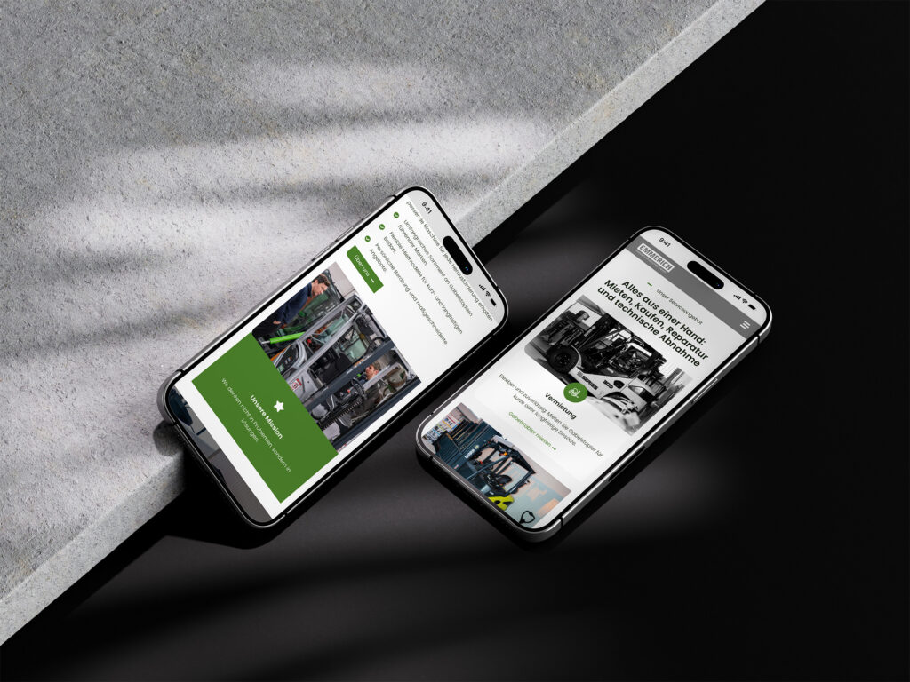 Zwei Smartphones liegen nebeneinander auf einer schwarz-grauen Fläche und zeigen beide eine Website mit Bildern von arbeitenden Menschen, grünen Akzenten und deutschem Text an. Die Telefone sind leicht angewinkelt und fangen Licht und Schatten ein.