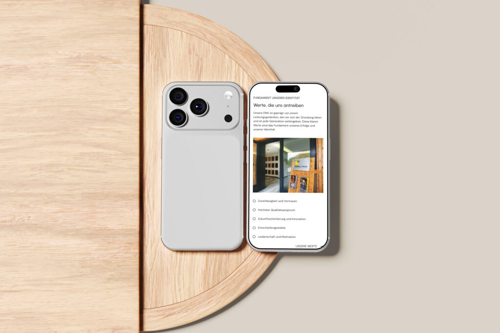 Ein weißes Smartphone mit einer Dreifachkamera liegt neben einem anderen Telefon, das eine Website-Umfrage in deutscher Sprache anzeigt. Beide liegen auf einem runden Holztisch vor einem beigen Hintergrund.