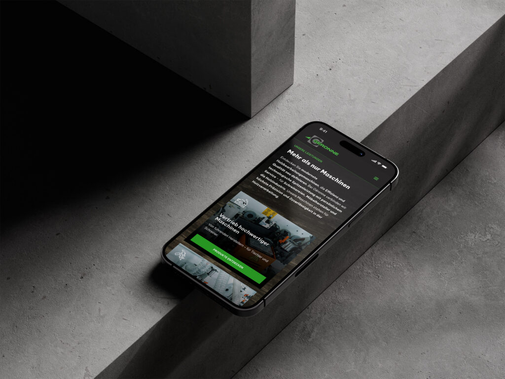 Ein Smartphone, das eine Website mit grünen Akzenten anzeigt, ruht auf einer Betonfläche, auf der Text, Bilder und Schaltflächen in deutscher Sprache zu sehen sind. Die Umgebung ist minimalistisch mit geometrischen Schatten.