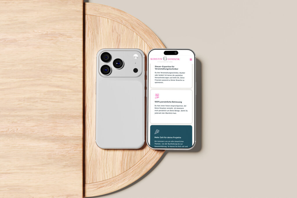 Ein weißes Smartphone mit Doppelkamera liegt auf einem runden Holztisch und zeigt auf seinem Bildschirm eine Website mit deutschem Text an. Der Tisch ist vor einem beigen Hintergrund aufgebaut.