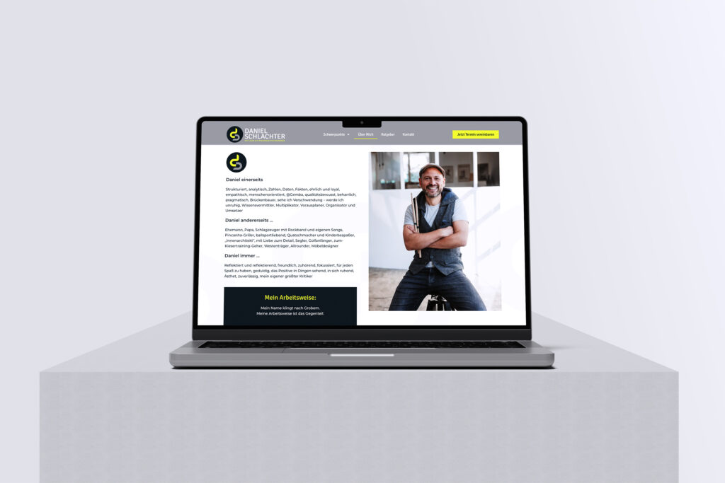 Ein Laptop auf einem grauen Sockel zeigt eine Website mit dem Foto eines lächelnden Mannes in einer Weste, der die Arme verschränkt, neben Text und einer gelben Schaltfläche auf einer sauberen, modernen Webseite.