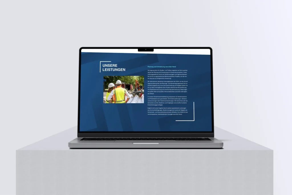 Ein Laptop auf einem weißen Sockel zeigt eine deutschsprachige Webseite mit blauem Hintergrund, einem Bild von Bauarbeitern und einem Text mit der Überschrift UNSERE LEISTUNGEN.