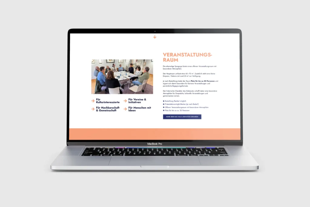 Auf einem MacBook Pro wird eine Website angezeigt, die ein Foto von Menschen zeigt, die sich an einem Tisch treffen, sowie Informationen zu Veranstaltungsorten auf Deutsch und Symbole für Kultur, Nachbarn und Ideen. Der Bildschirm weist ein weiß-orangefarbenes Layout auf grauem Hintergrund auf.