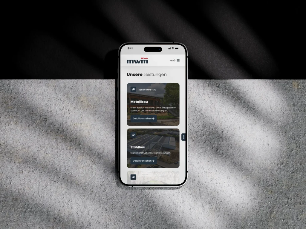 Ein Smartphone, auf dem eine Website auf Deutsch mit Rubriken zu Metallbau und Stahlbau angezeigt wird, liegt auf einer strukturierten Oberfläche und wird teilweise von gestreiften Schatten beleuchtet.