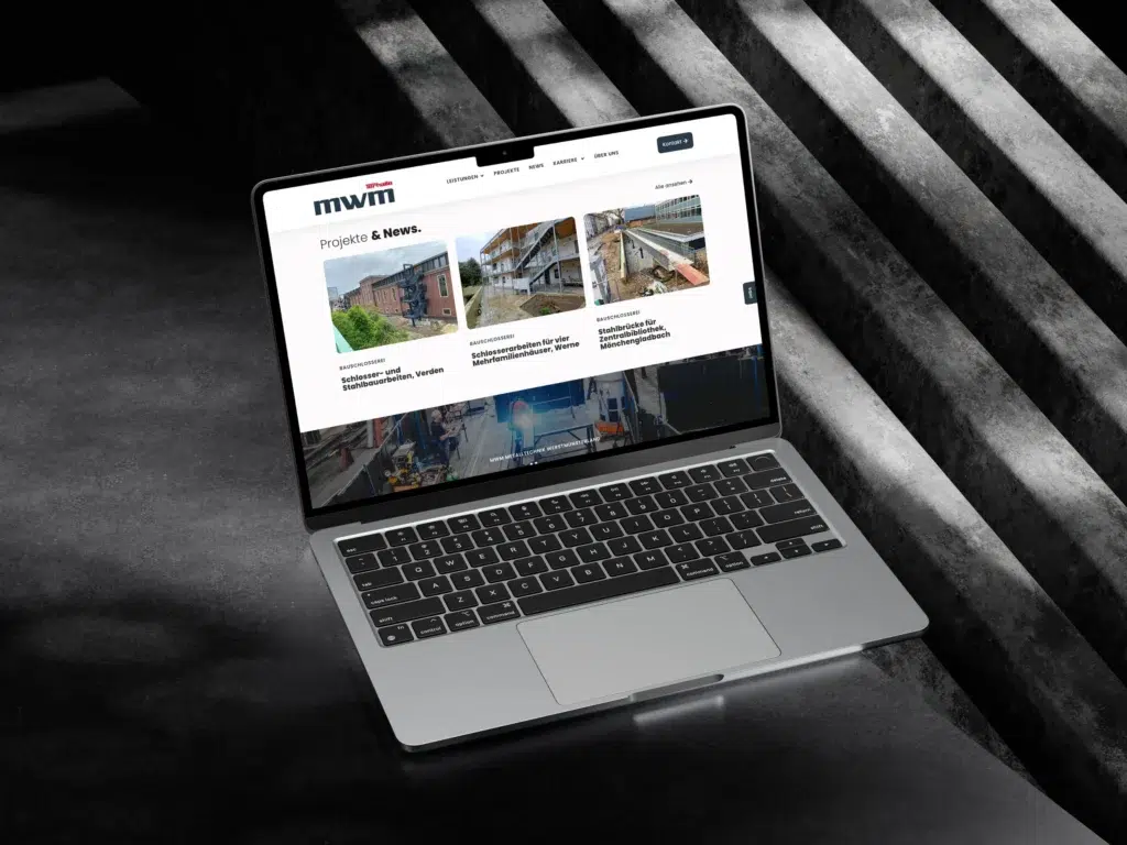 Auf einem Laptop, der auf einer dunklen Treppe steht, ist eine Website mit dem mwm-Logo, einem Navigationsmenü und Bildern von Bauprojekten unter der Überschrift „Projekte & News“ zu sehen.