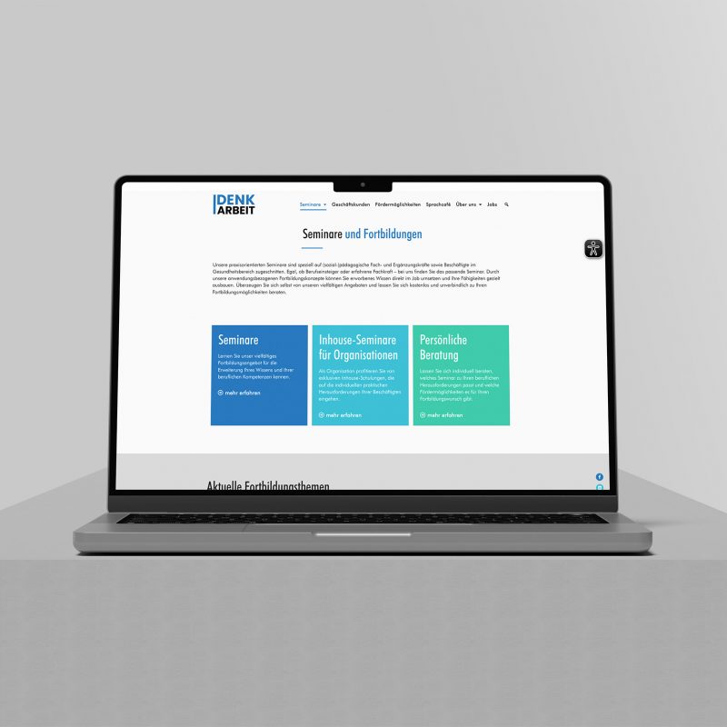 Ein Laptop auf einer grauen Plattform zeigt die DenkArbeit.Ruhr-Website mit weißem Hintergrund, blauen Akzenten und drei farbigen Kästen mit den Bezeichnungen "Seminare", "Inhouse-Seminare für Organisationen" und "Persönliche Beratung".