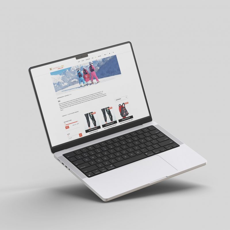 Ein silberner Laptop schwebt vor einem hellgrauen Hintergrund und zeigt den Sanitätshaus M+L Online-Shop mit Winterbekleidung wie Jacken und Mänteln, wobei die Produktbilder und -informationen auf dem Bildschirm gut sichtbar sind.
